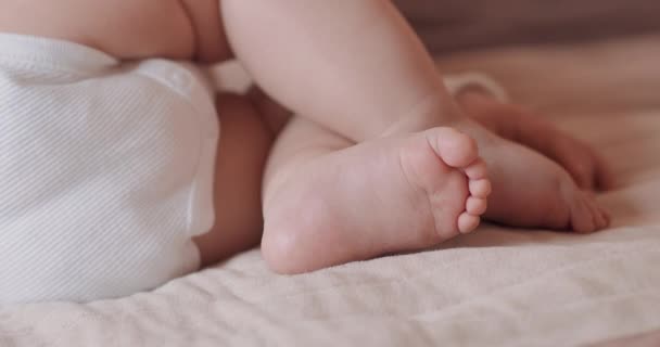 Cerca de los pies de un hermoso bebé dormido, desnudo, en pañales, en la cama — Vídeos de Stock