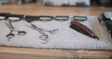 Gri havludaki budama makinesi, jilet, berber makası ve bulanık budama eklentileri, ahşap masadaki kamera sağa sola gidiyor.