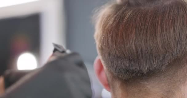 Detailní záběr ženských holičských rukou, které stříhají střihačem vlasů a česají mladé vousaté muže, kteří sedí na holičské židli zády k ní, čelem k zrcadlu — Stock video
