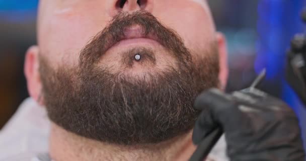 Bărbia de aproape a tânărului bărbat cu barbă, cu inel de bărbie și mâini de bărbierit de sex feminin, care își taie barba cu fundal blurred tuns — Videoclip de stoc
