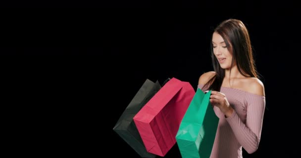 Jeune fille caucasienne 20s ans en robe rose décontractée tenir dans les mains regarder dans les sacs de paquet avec des achats après les achats isolés sur fond noir studio Personnes concept de style de vie — Video