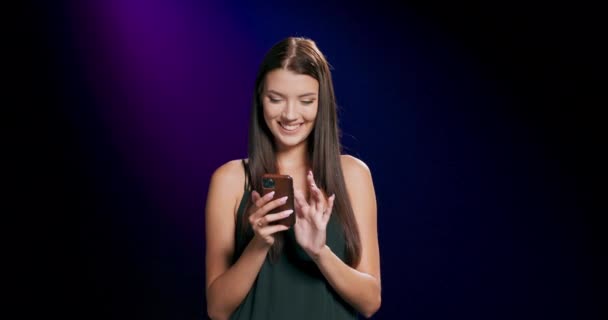 En kvinna som kollar sin smartphone när hon står mot en lila och svart bakgrund — Stockvideo