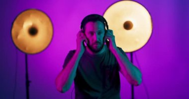 Kulaklıklı genç bir adamın portresi, stüdyo arka planında renkli parlak neon ışıklarla kaslı stüdyo erkek modelinin ritmine göre hareket ediyor.