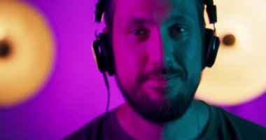 Kulaklıklı genç bir adamın portresi, stüdyo arka planında renkli parlak neon ışıklarla kaslı stüdyo erkek modelinin ritmine göre hareket ediyor.