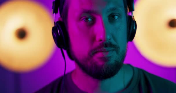 Ritratto di un giovane uomo in cuffia, che si muove al ritmo dello studio musicale Modello maschile in luci al neon luminose colorate in posa sullo sfondo dello studio — Video Stock