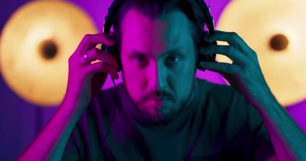 Portret młodego mężczyzny noszącego słuchawki podczas patrzenia w kamerę Mężczyzna model w kolorowych jasnych neonach pozujących na tle studia — Wideo stockowe