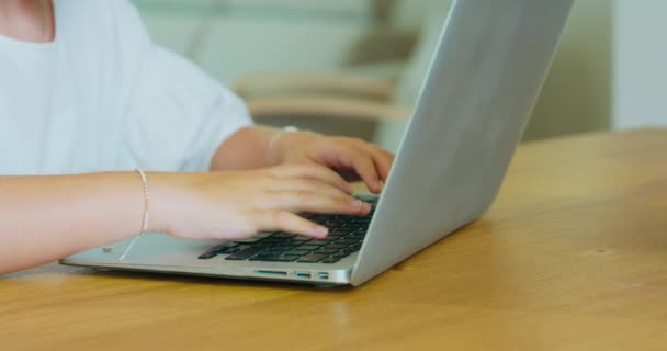 Крупный план руки девочки-подростка, с браслетами на запястьях, запись на ноутбуке на столе — стоковое видео