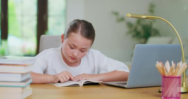 Menina adolescente focada na mesa, lê um livro, linhas de rastreamento com dedo Laptop de lado Livros, cadernos, lápis, laptop, lâmpada no primeiro plano fora de foco Backgroung é borrado — Vídeo de Stock