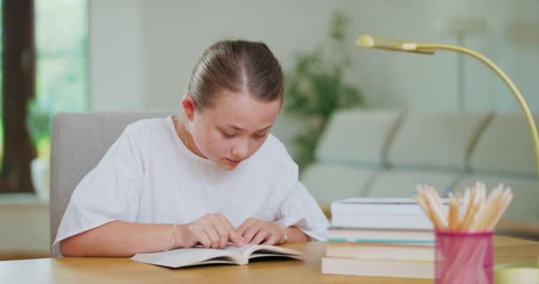 Menina adolescente focada na mesa, lê um livro, linhas de rastreamento com dedo Livros, cadernos, lápis, laptop, lâmpada no primeiro plano fora de foco Backgroung é borrado — Vídeo de Stock