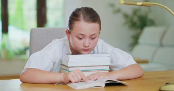 Menina adolescente focada na mesa, lê um livro, linhas de rastreamento com o dedo, descansando o queixo na pilha de livros Backgroung é turvo — Vídeo de Stock