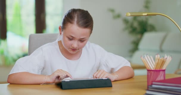 Enfocado chica adolescente en el escritorio, la tableta de desplazamiento Libros, lápices y lámpara en el primer plan Primer plan y backgroung son borrosas — Vídeos de Stock