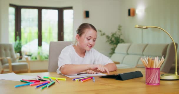 Fokuserad tonåring flicka, vid skrivbordet, rullar tablett, sträcker sedan upp händerna Filtspets pennor, vitt papper, tablett, pennor, böcker lampa på skrivbordet Väggar, fönster på bakgrunden är suddig — Stockvideo