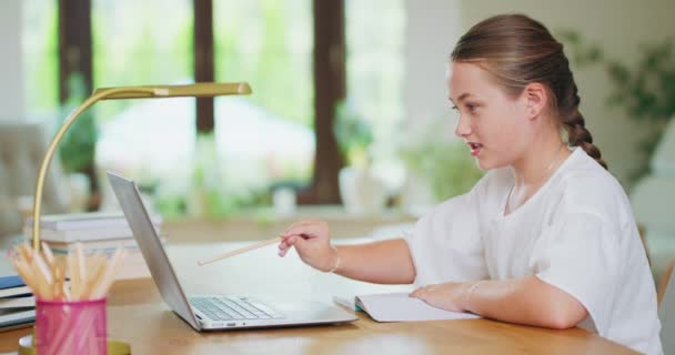 Gesloten gericht tienermeisje, aan het bureau, schrijft taken in notebook en controleert ze op laptop Boeken, notebooks, potloden, lamp uit beeld Achtergrond is wazig Foto van opzij — Stockvideo