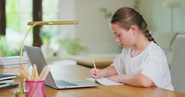 Zamknięte skupione nastolatka dziewczyna, przy biurku, pisze zadania w notebooku i sprawdza je na laptopie Książki, notebooki, ołówki, lampa nieostre Tło jest zamazane Zdjęcie z boku — Wideo stockowe