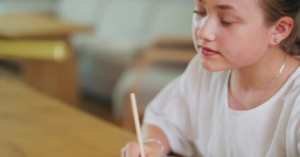 Закрытая целеустремленная девочка-подросток, за столом, выполняет задания в рабочей тетради и проверяет их на ноутбуке Фон размыт — стоковое видео