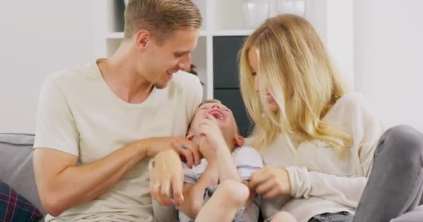 Cariñoso caucásico padre y madre cosquillas pequeño adorable hijo teniendo divertido riendo relajarse en sofá, polaco padres jugando con pequeño niño niño vinculación abrazos juntos en casa — Vídeos de Stock