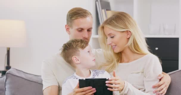 Hermosos padres jóvenes y su pequeño hijo lindo están utilizando una tableta digital y sonriendo mientras pasan tiempo juntos — Vídeos de Stock