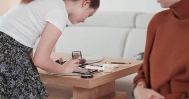 Genç kız annesine makyaj yapmayı öğreniyor. Paletteki göz gölgelerini seçiyor ve annesi ona nasıl yapması gerektiğini söylüyor.