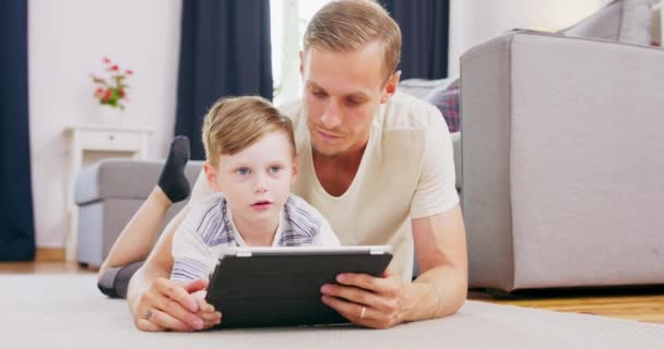 Szczęśliwa młoda europejska rodzina leżąca na dywanie z małym dzieckiem oglądać kreskówki na tablecie, szczęśliwy biały rodzic bawić relaks z chłopcem dziecko na diwanie cieszyć się wideo na pad spędzać czas w domu razem — Wideo stockowe