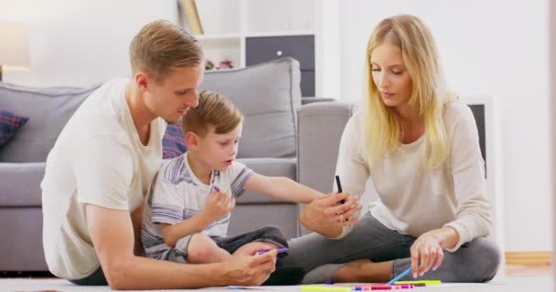 Kochający rodzice rodziny z cute dziecko syn cieszyć się rysunek z markerów kolorowanki obraz siedzi na podłodze, szczęśliwy tata mama i mały chłopiec uśmiecha się bawiąc się razem w domu w salonie — Wideo stockowe