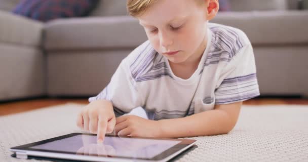 Mały chłopiec w ekspresyjnej twarzy przy użyciu tabletu cyfrowego na podłodze Chłopiec bawiący się tabletem cyfrowym Portret małego dziecka w domu oglądającego kreskówkę na urządzeniu mobilnym Nowoczesne dziecko i edukacja — Wideo stockowe