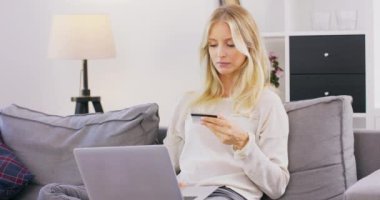 Özenli bir kadın evinde rahat bir koltukta dizlerinin üzerine çöküp internette geziniyor, mutlu bir kız haftasonunu kanepede dinlenerek ve online alışveriş yaparak geçiriyor.