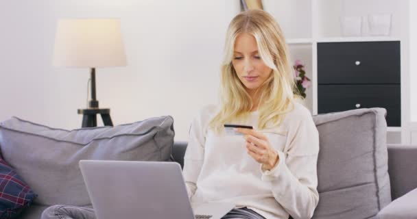 Mujer sonriente y feliz sentado en el sofá en la sala de estar de compras en línea en el ordenador portátil Bastante caucásica chica de mediana edad que gasta dinero de la tarjeta de crédito durante las compras en línea — Vídeo de stock