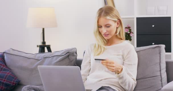 Uśmiechnięta i szczęśliwa kobieta siedzi na kanapie w salonie robiąc zakupy online na laptopie Całkiem kaukaska dziewczyna w średnim wieku wydająca pieniądze z karty kredytowej podczas zakupów online — Wideo stockowe