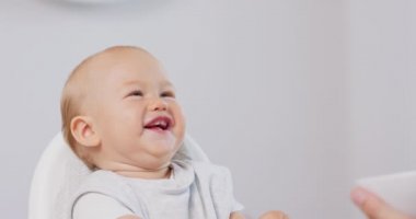 Beyaz bebek sandalyesinde küçük bir bebeğin resmi ve kaşıkla babalar ellerini beslerken, o da gülüyor, yiyor ve arka planda beyaz duvarlar yapıyor.