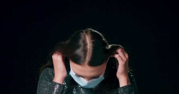 Nahaufnahme eines jugendlichen kaukasischen Mädchens im Brokatkleid, das eine medizinische Schutzmaske vor schwarzem Studiohintergrund mit Kopierraum aufsetzt — Stockvideo