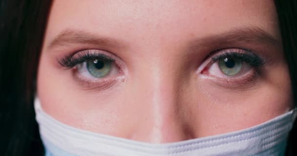 Tıbbi yüz maskesi takan bir kadının kameraya baktığı gözlere yakından bakın. — Stok video
