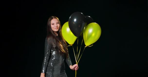 En pige iført en sort brokade kjole danser alene og holder sorte og guld balloner i hånden – Stock-video
