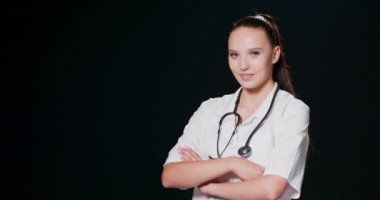 Kendine güvenen doktor kollarını kavuşturmuş gülümseyen genç kadın doktor stajyer doktor beyaz elbiseli güzel kadın fonendoskopla poz veriyor ve gülümsüyor.