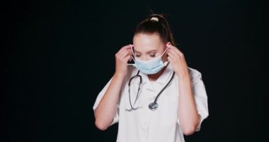 Koruyucu tıbbi yüz maskesi takan bir kadın kameraya bakıyor kadın doktor portresi düz görünüyor, siyah arka plana karşı poz veriyor, boşluğu kopyalıyor.