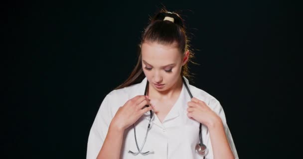 Hovedbillede portræt af smilende tusindårig kvindelig læge iført medicinsk uniform og stetoskop ser på kameraet, glad ung kvinde alment praktiserende læge eller sygeplejerske udgør i hvid, sundhedspleje koncept – Stock-video