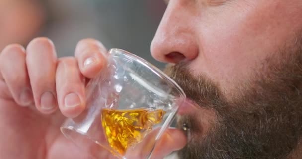 Großaufnahme Gesicht eines jungen bärtigen Mannes, mit Kinnring, trinkt Whisky in schädelförmigem Glas Mann blickt direkt vor sich Hintergrund verschwommen — Stockvideo