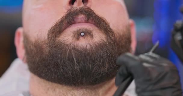 Detailní brada mladého vousatého muže, s bradu kroužek, a ženské ruce holiče, který řeže vousy s zastřihovačem rozmazané pozadí — Stock video