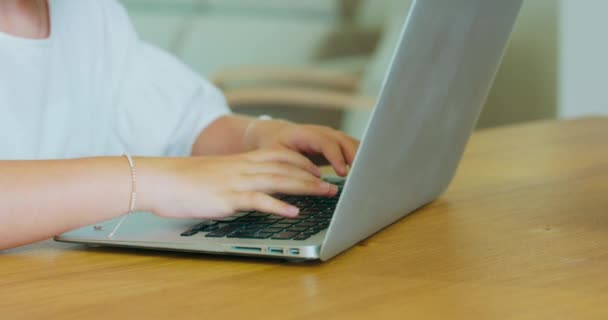 Primeros planos de las manos de la chica adolescente, con pulseras en las muñecas, la escritura en el ordenador portátil está en la mesa — Vídeos de Stock