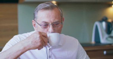 Lezzetli bir içecek. Mutfaktaki sandalyede oturan gözlüklü hoş yaşlı adam.