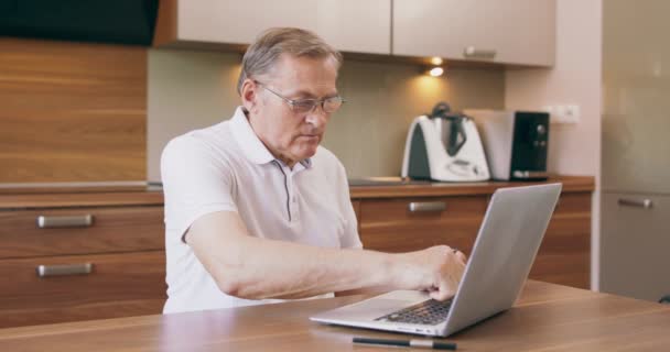现代老年人在网上购物或在家里厨房使用笔记本电脑时支付信用卡税金的温暖写真 — 图库视频影像
