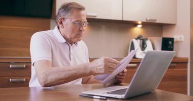 Avrupalı Kafkasyalı kafası karışık ve kıdemli bir adam internet faturalarını dizüstü bilgisayarla ödüyor