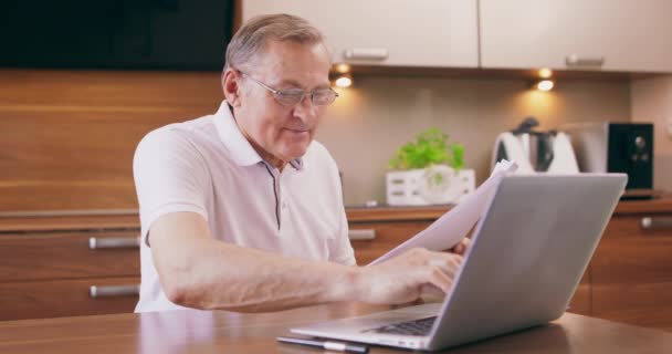 Homem idoso feliz sentado na cadeira na cozinha e comprando com laptop usar site on-line, voucher e cartão de crédito bancário reserva hotel plano férias, homem velho aprendendo sistema de pagamento na internet — Vídeo de Stock