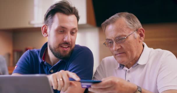 Mężczyzna uczy ojca jak robić zakupy online Wnuczka pokazuje dziadkowi jak poprawnie wpisywać numery kart kredytowych w sklepie internetowym — Wideo stockowe