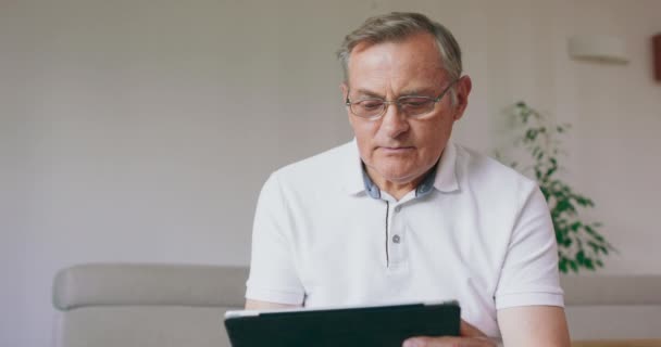 Um homem sênior aprende a usar seu novo computador tablet digital Homem sênior censurado lendo notícias no tablet digital Homem maduro animado alegre usando o computador portátil em casa — Vídeo de Stock