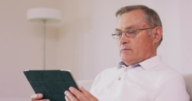 Büyükbabanın tablet bilgisayar kullanırken çekilmiş bir fotoğrafı. Teknoloji kullanıyor. Kanepede oturan yaşlı adamın portresi.