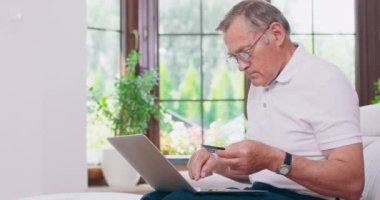 Yaşlı bir adam internet üzerinden bir şeyler ödemek için banka kartını kullanıyor.