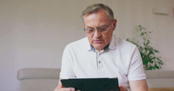 Пожилой человек садится, чтобы научиться пользоваться своим новым планшетом. — стоковое видео