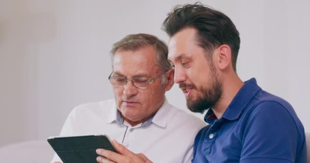 Κοντινό πλάνο ενός ηλικιωμένου που διδάσκεται από το γιο του πώς να χρησιμοποιεί έναν υπολογιστή tablet Η εγγονή δείχνει στον παππού πώς να εισάγει σωστά τους αριθμούς πιστωτικών καρτών στο ηλεκτρονικό κατάστημα — Αρχείο Βίντεο