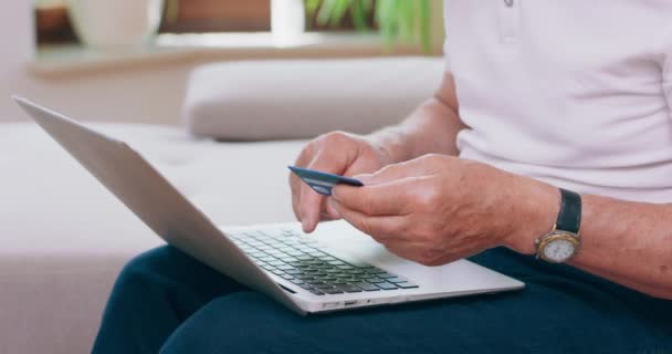 Primer plano de una mano escribiendo en un teclado portátil Un hombre mayor utiliza su tarjeta de débito para pagar algo en línea con su computadora portátil — Vídeo de stock