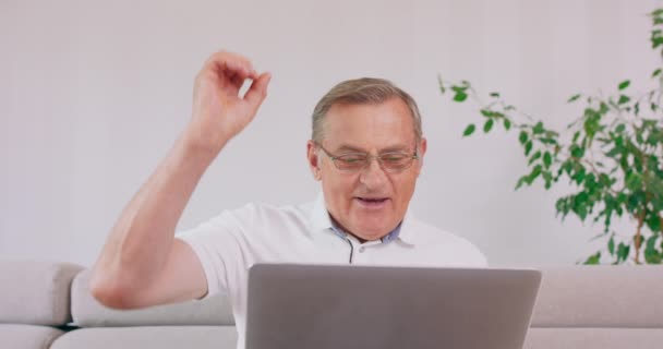 An elderly man with a laptop computer cheers upon reading good news — Stock Video